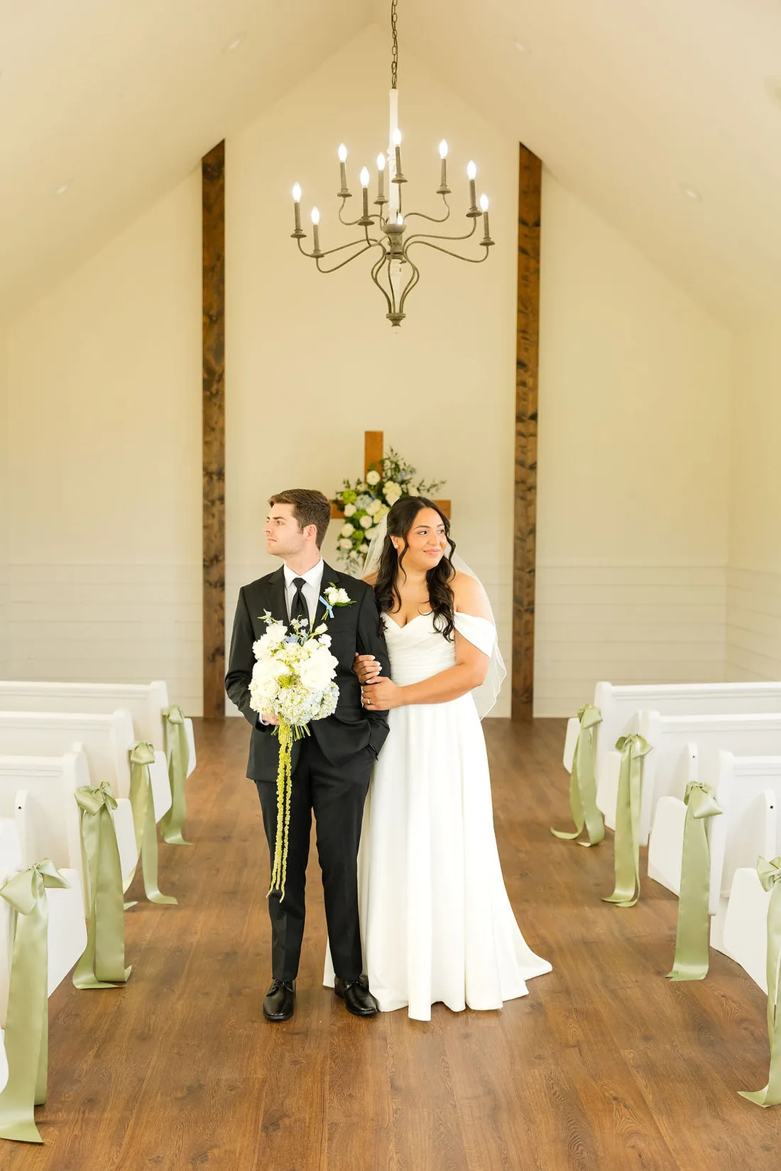 Jennifer and Hayden in the chapel aisle with sage pew florals at Gateley Hill Gardens