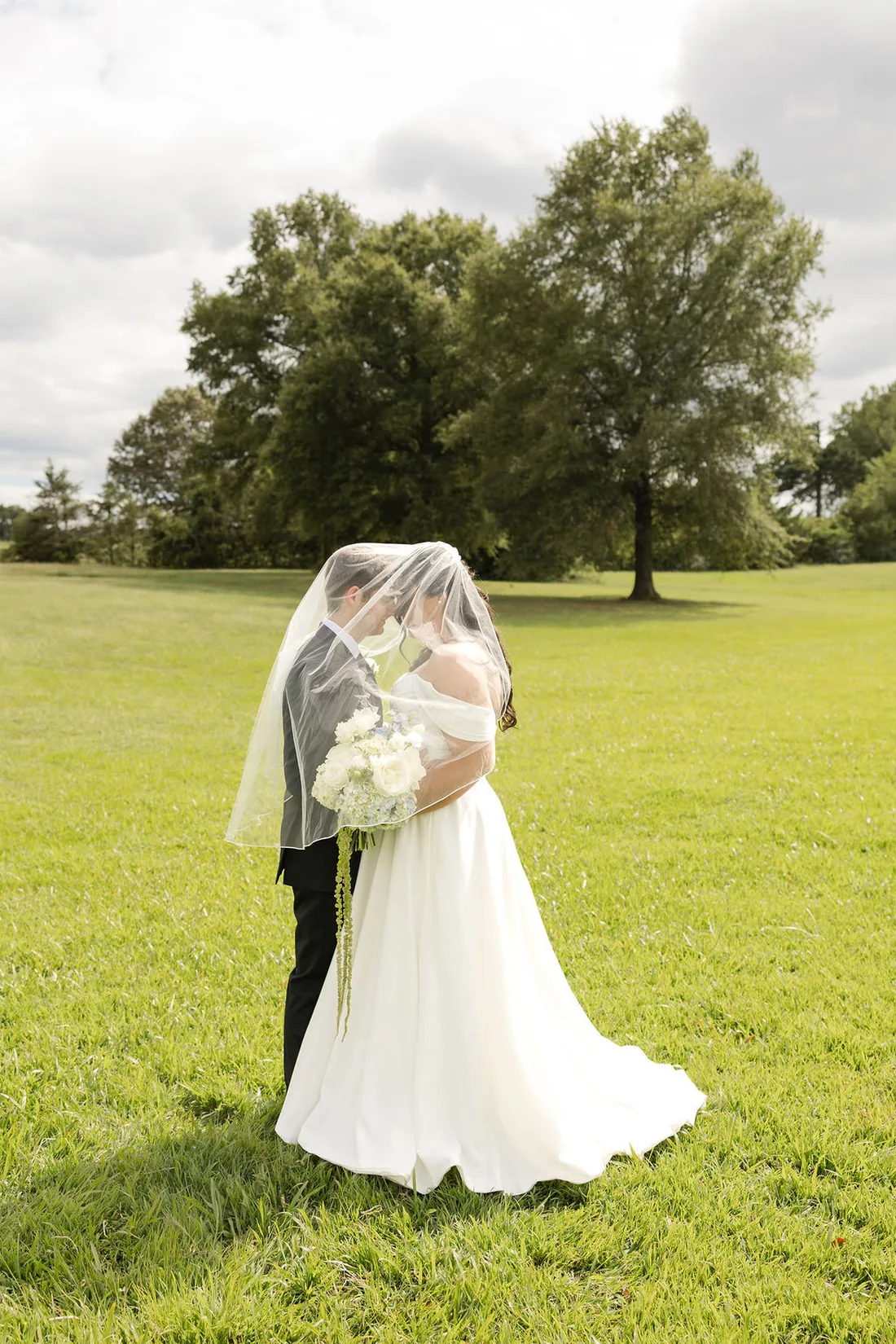 Jennifer and Hayden kissing under her veil in the field at Gateley Hill Gardens