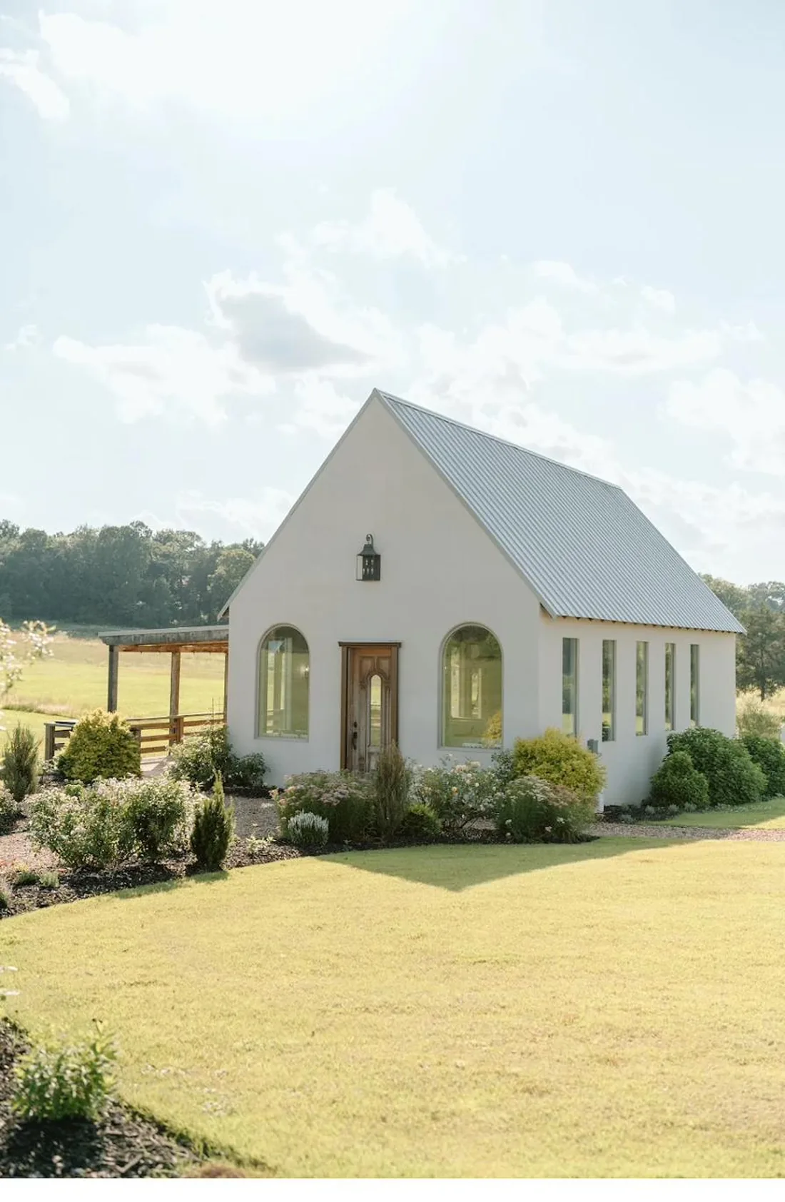 White stucco chapel on a green spring lawn with blooming flower beds at Gateley Hill Gardens